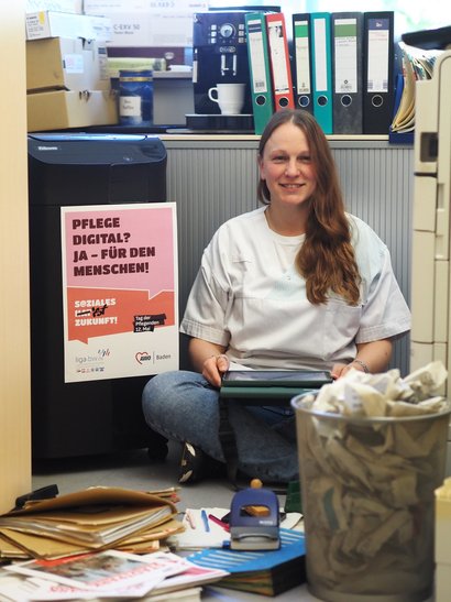 Pflegefachkraft sitzt anlässlich des Aktionstages Tag der Pflegenden in einem Berg voller Akten