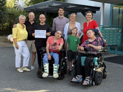 Einrichtungsleiter Niko Körper hält einen Spendenscheck, um ihn herum eine Gruppe von Menschen.