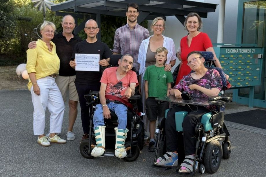 Einrichtungsleiter Niko Körper hält einen Spendenscheck, um ihn herum eine Gruppe von Menschen.