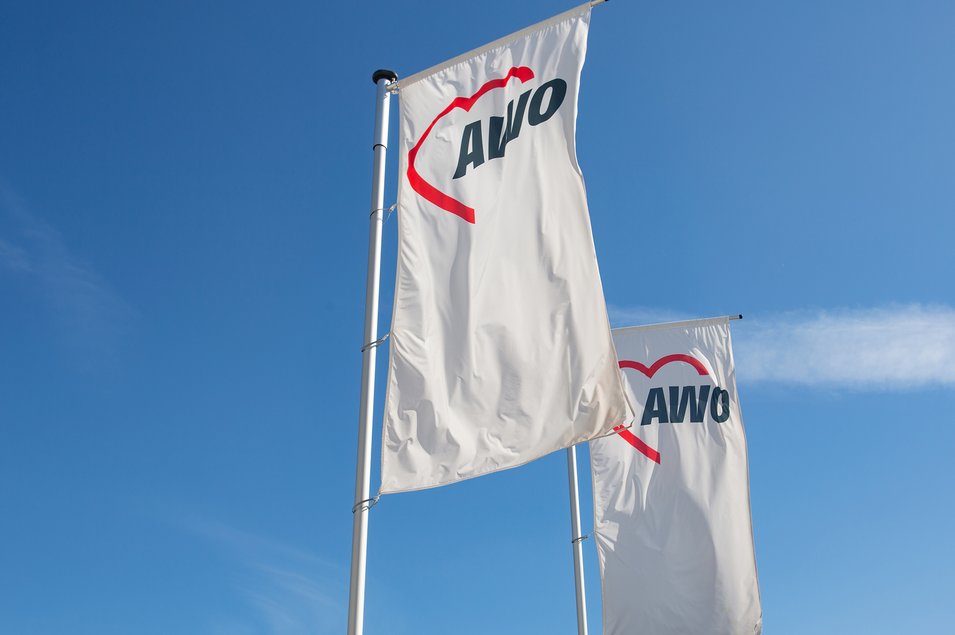 zwei weiße AWO-Fahnen wehen vor einem blauen Himmel