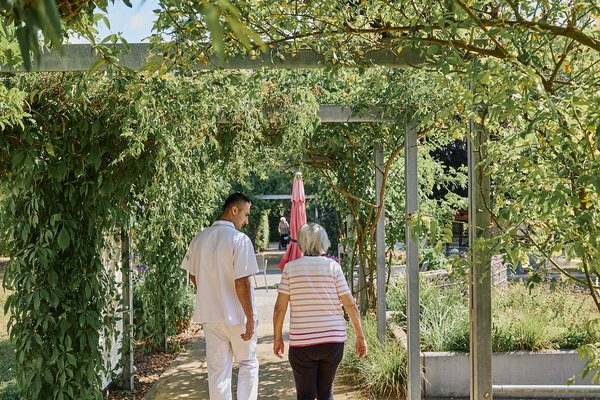 Pflegefachkraft und Bewohnerin spazieren im Garten