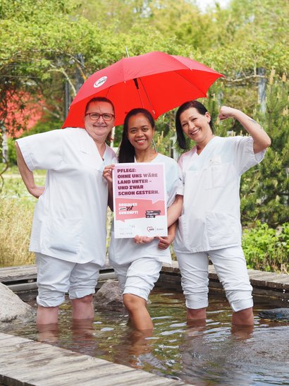 Drei Pflegefachkräfte stehen in einem wassergefüllten Becken anlässich der Kampagne Tag der Pflegenden