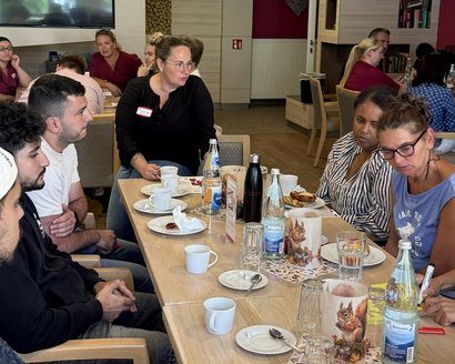 Teilnehmende einer Kick-off-Veranstaltung arbeiten gemeinsam an Aufgaben und tauschen sich in Kleingruppen an einem Tisch aus.